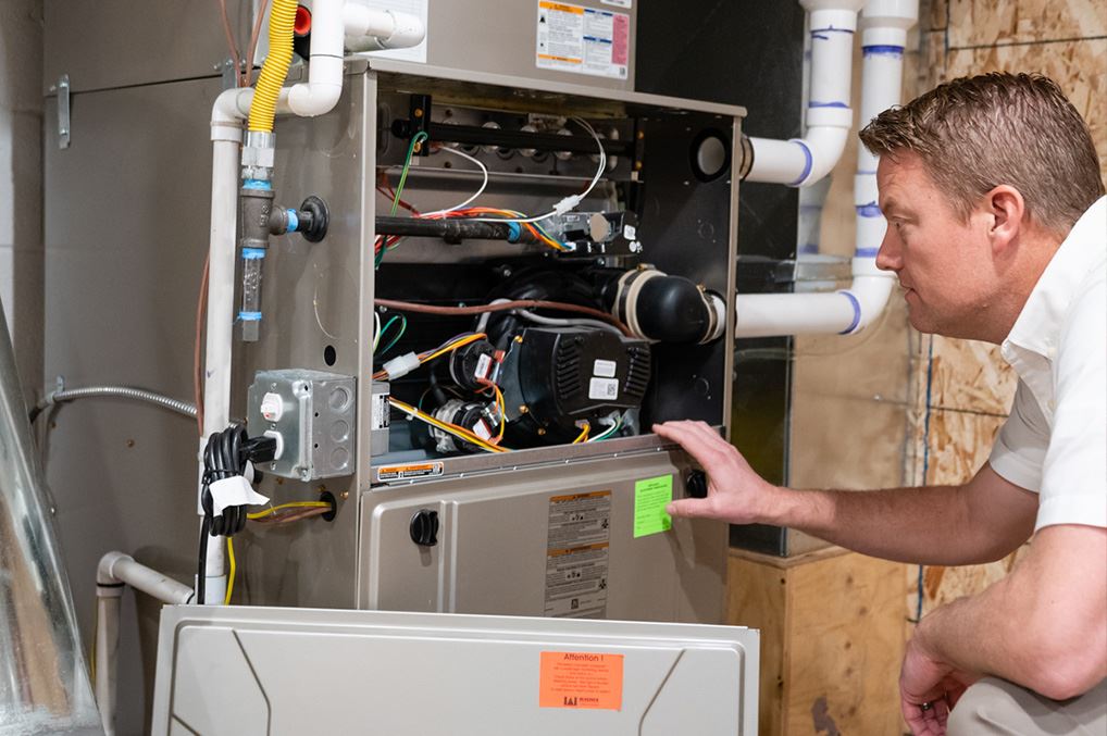 This image depicts a man, likely an HVAC technician, inspecting the open cabinet of a residential gas furnace.